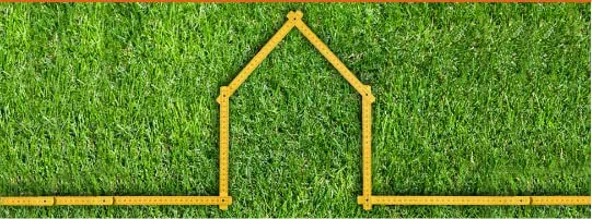A yellow foldable ruler arranged in the shape of a house on a green grass background.