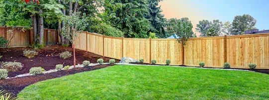 A well-maintained backyard with a wooden fence, green lawn, and landscaped garden beds